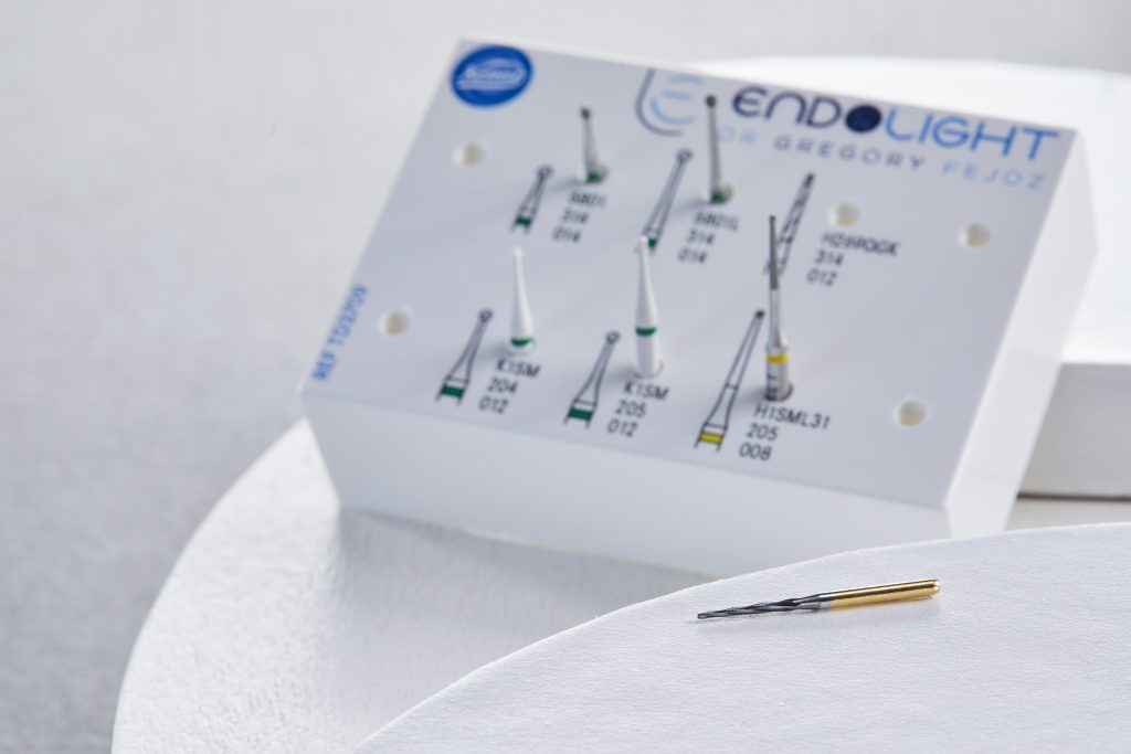 Fraise longue en carbure dorée posée sur une surface blanche, devant le kit de fraises de pulpotomie Endolight, utilisée pour l’élimination efficace de tissus durs